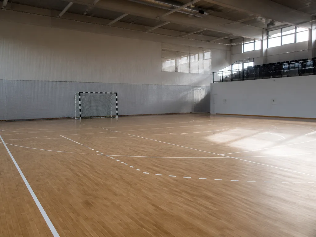Tom handbollsplan i en idrottshall med vita linjer, målgårdslinje och ett handbollsmål med nät